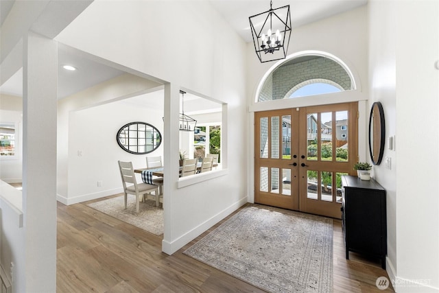entrance foyer featuring baseboards, a towering ceiling, a notable chandelier, and wood finished floors