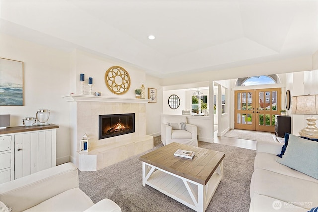 carpeted living area with baseboards, a raised ceiling, a fireplace, recessed lighting, and french doors