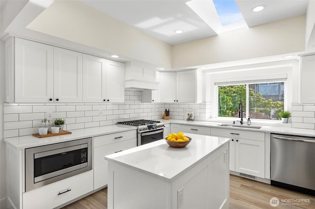 kitchen featuring light wood-type flooring, a skylight, a sink, stainless steel appliances, and decorative backsplash