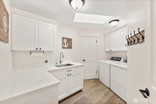 laundry room with light wood-style flooring, a skylight, a sink, cabinet space, and washer and clothes dryer