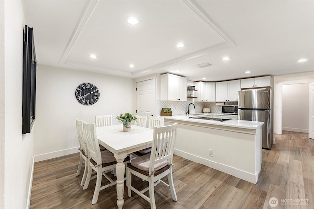 dining area featuring recessed lighting, light wood-type flooring, a tray ceiling, and baseboards