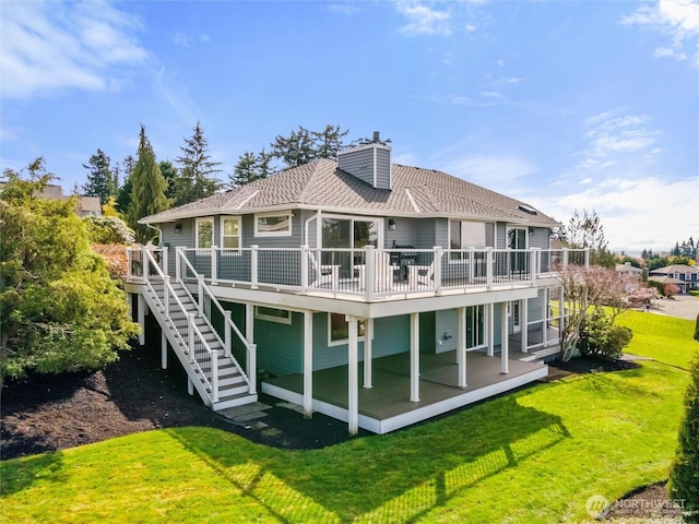 back of property with stairway, a wooden deck, a chimney, and a lawn
