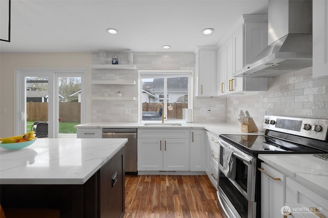 kitchen featuring dark wood-style floors, open shelves, wall chimney exhaust hood, appliances with stainless steel finishes, and a sink