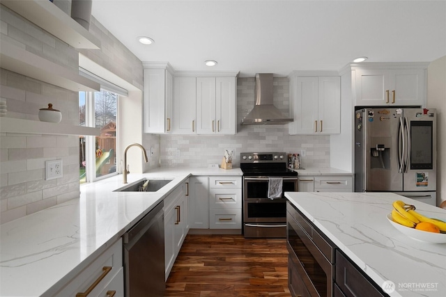 kitchen featuring wall chimney exhaust hood, a sink, white cabinetry, light stone countertops, and stainless steel appliances