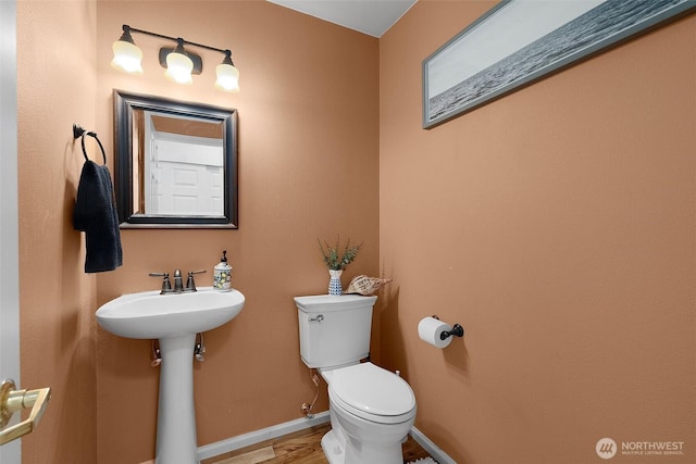 half bath with toilet, wood finished floors, a sink, and baseboards