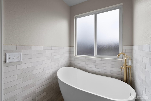 bathroom with tile walls, a freestanding tub, and a wainscoted wall