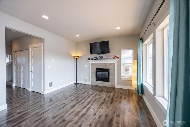 unfurnished living room with a stone fireplace, baseboards, recessed lighting, dark wood-type flooring, and visible vents