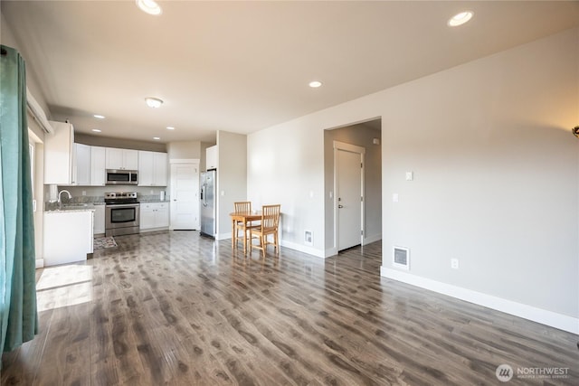 unfurnished living room with baseboards, dark wood-type flooring, a sink, and visible vents