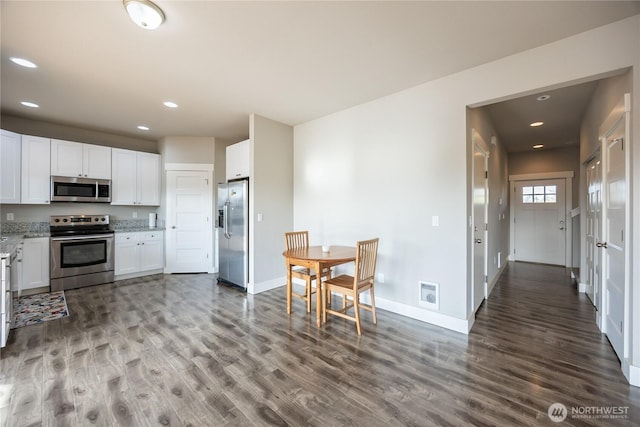 kitchen with baseboards, white cabinets, light stone countertops, stainless steel appliances, and wood finished floors