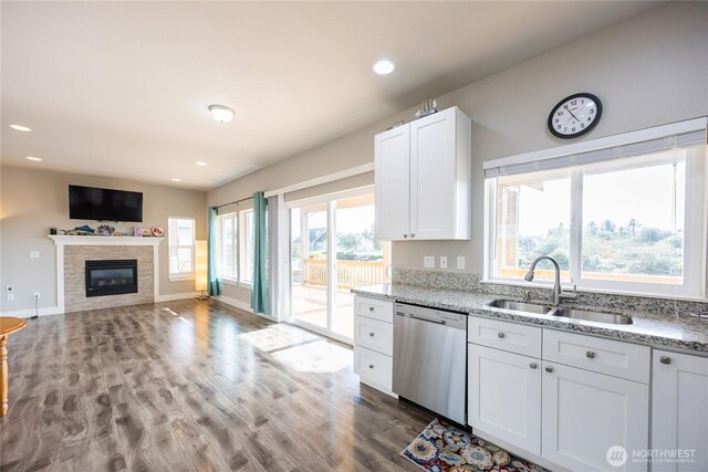 kitchen featuring white cabinetry, light stone countertops, dishwasher, a sink, and wood finished floors