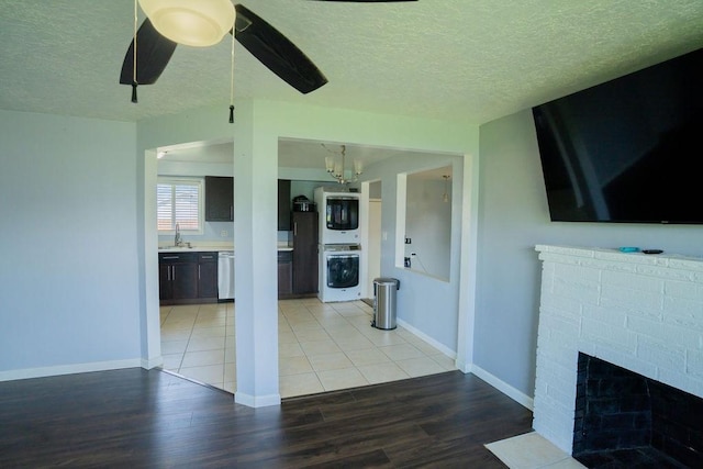 unfurnished living room featuring light wood-style flooring, a textured ceiling, a sink, baseboards, and stacked washer / drying machine