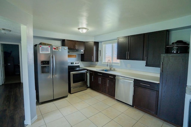 kitchen featuring dark brown cabinetry, appliances with stainless steel finishes, under cabinet range hood, light countertops, and a sink
