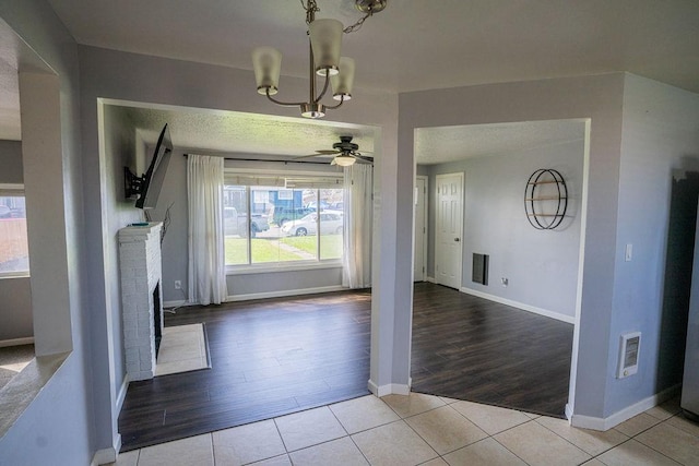 unfurnished dining area featuring ceiling fan with notable chandelier, a fireplace, visible vents, tile patterned floors, and baseboards