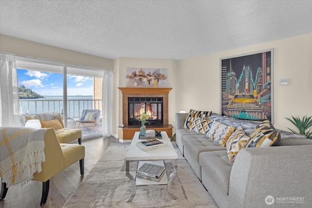 living area with a glass covered fireplace, wood finished floors, a textured ceiling, and a water view