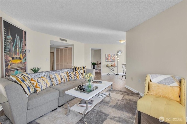 living room featuring a textured ceiling, wood finished floors, visible vents, and baseboards