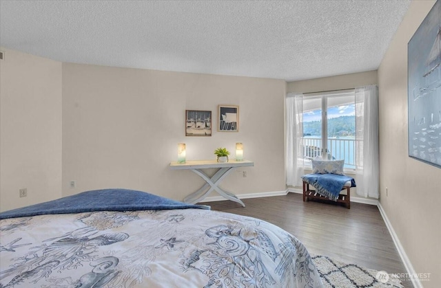 bedroom featuring wood finished floors, a textured ceiling, a water view, baseboards, and access to outside