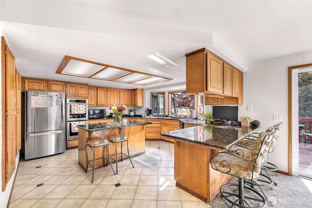 9652 Ronald Dr, Blaine, WA 98230 - kitchen with appliances with stainless steel finishes, brown cabinetry, dark stone counters, a peninsula, and a kitchen bar
