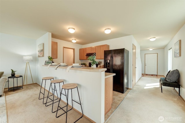 kitchen with light colored carpet, a peninsula, black fridge, and a kitchen bar