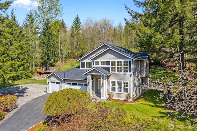 view of front of house featuring an attached garage, a view of trees, driveway, and a front lawn