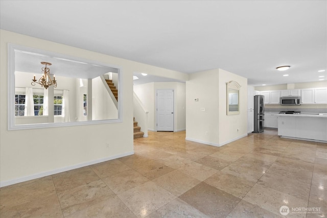 unfurnished living room featuring a chandelier, recessed lighting, baseboards, and stairway