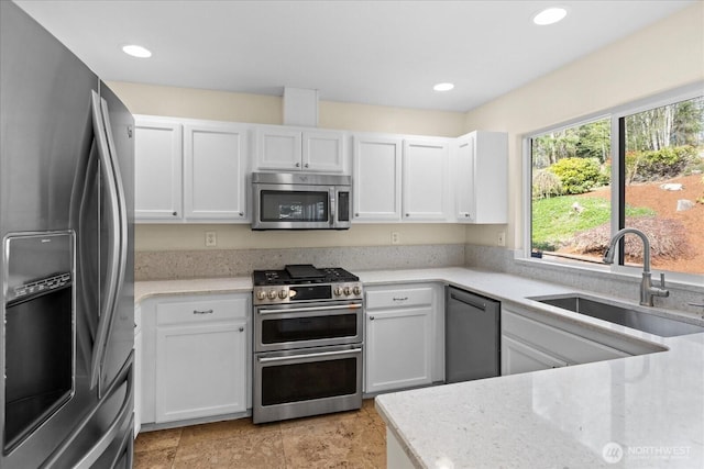 kitchen with a sink, appliances with stainless steel finishes, light stone counters, and white cabinetry