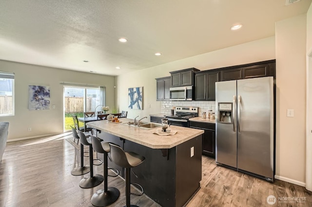 kitchen with a breakfast bar area, a center island with sink, a sink, light wood-style flooring, and appliances with stainless steel finishes