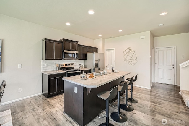 kitchen featuring a breakfast bar area, appliances with stainless steel finishes, light wood-type flooring, light countertops, and an island with sink