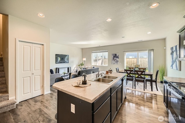 kitchen with electric range, open floor plan, light countertops, a sink, and light wood-style flooring