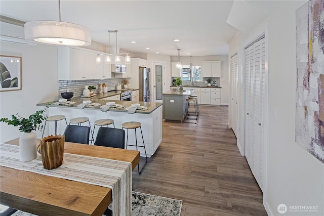 kitchen with a sink, a breakfast bar area, stainless steel appliances, backsplash, and dark wood-style floors