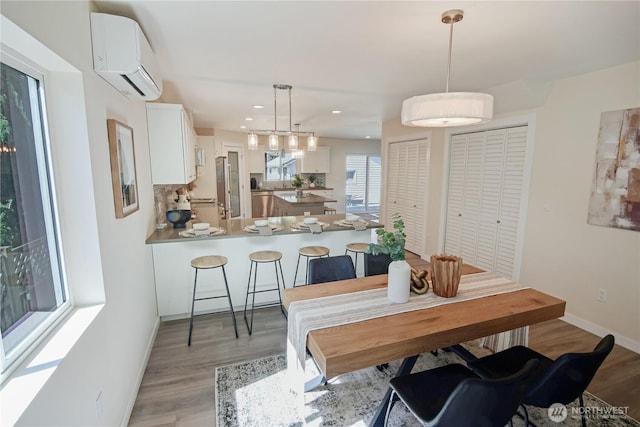 dining space featuring light wood finished floors, baseboards, an AC wall unit, and recessed lighting