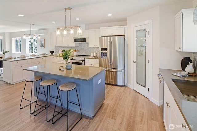 kitchen featuring white cabinets, light wood finished floors, a kitchen breakfast bar, a peninsula, and appliances with stainless steel finishes