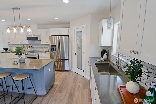 kitchen featuring white cabinets, stainless steel appliances, a sink, tasteful backsplash, and a breakfast bar area