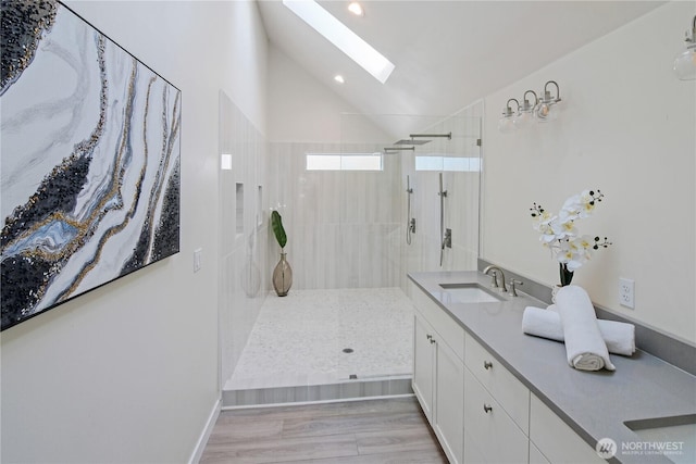 full bathroom featuring walk in shower, vaulted ceiling with skylight, vanity, and wood finished floors