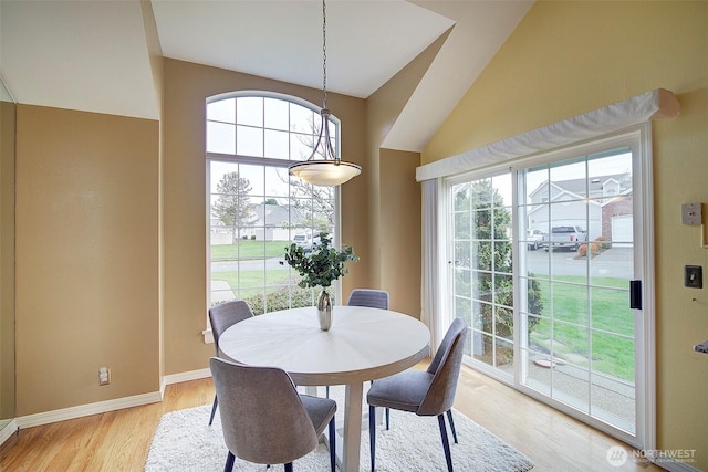 dining area with light wood-style flooring, baseboards, and vaulted ceiling