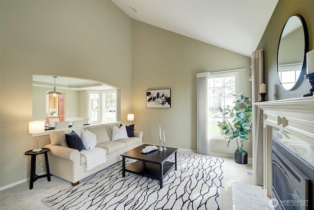 carpeted living area with high vaulted ceiling, arched walkways, and baseboards