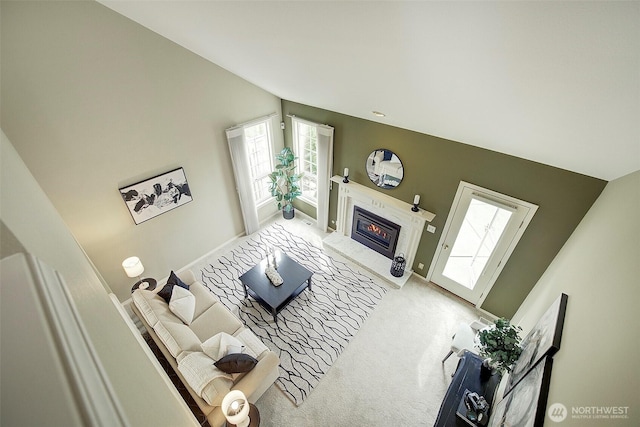living room featuring baseboards, vaulted ceiling, a glass covered fireplace, and a healthy amount of sunlight