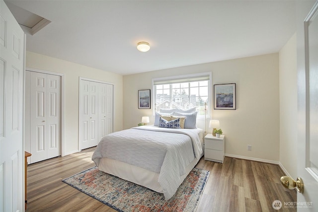 bedroom featuring baseboards, multiple closets, and wood finished floors