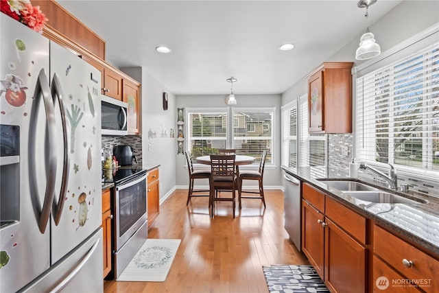 kitchen with appliances with stainless steel finishes, dark stone countertops, light wood-style flooring, decorative backsplash, and a sink