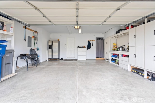 garage with a garage door opener, stainless steel refrigerator with ice dispenser, and electric panel