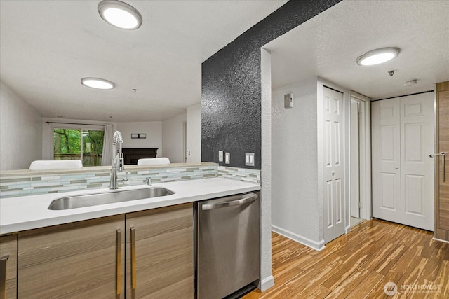 kitchen with dishwasher, a sink, a textured wall, light wood-style flooring, and light countertops