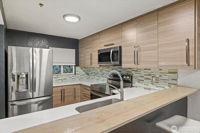 kitchen with stainless steel appliances, tasteful backsplash, light countertops, a sink, and a textured wall