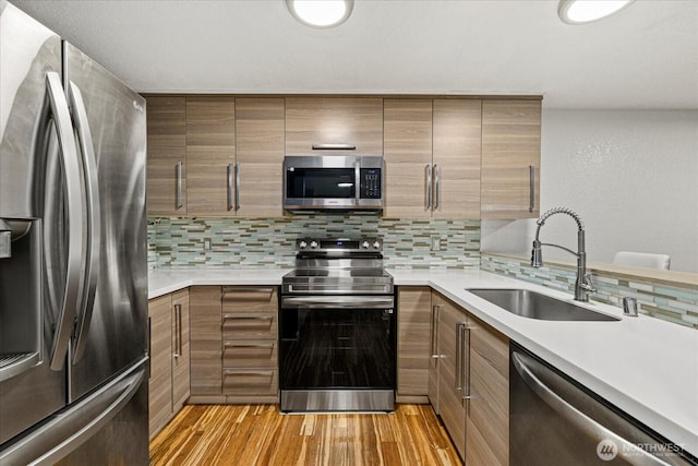 kitchen featuring appliances with stainless steel finishes, a sink, backsplash, light wood-style flooring, and light countertops