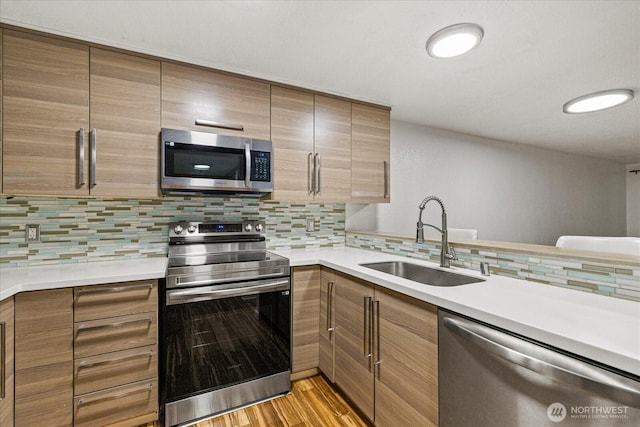 kitchen featuring appliances with stainless steel finishes, a sink, tasteful backsplash, and light countertops