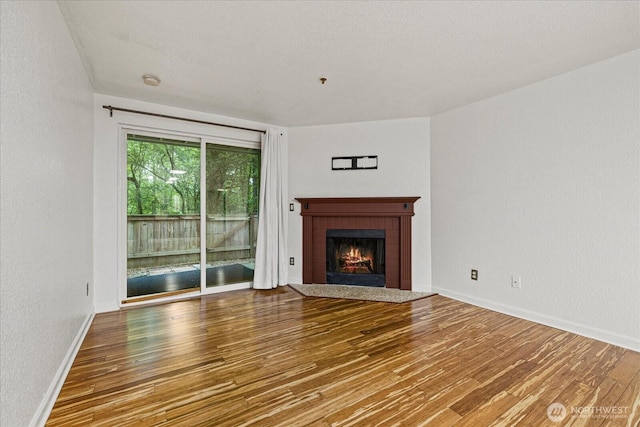 unfurnished living room featuring wood finished floors, a brick fireplace, a textured wall, and baseboards