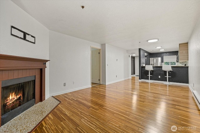 unfurnished living room with a tiled fireplace, wood-type flooring, baseboards, and a textured ceiling