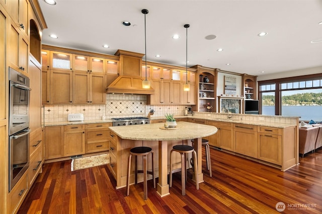 kitchen with glass insert cabinets, a peninsula, custom exhaust hood, appliances with stainless steel finishes, and a sink