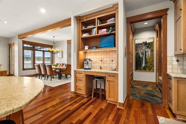 kitchen featuring dark wood-type flooring, an inviting chandelier, light stone counters, and decorative backsplash
