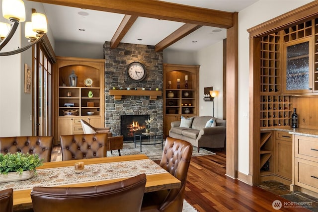 dining room featuring beamed ceiling, an inviting chandelier, a fireplace, dark wood-style flooring, and built in shelves