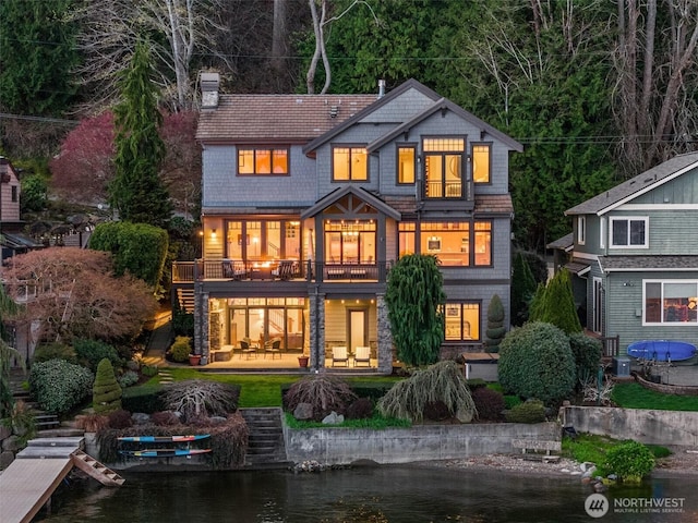 back of property featuring a chimney, a patio area, a water view, and a balcony