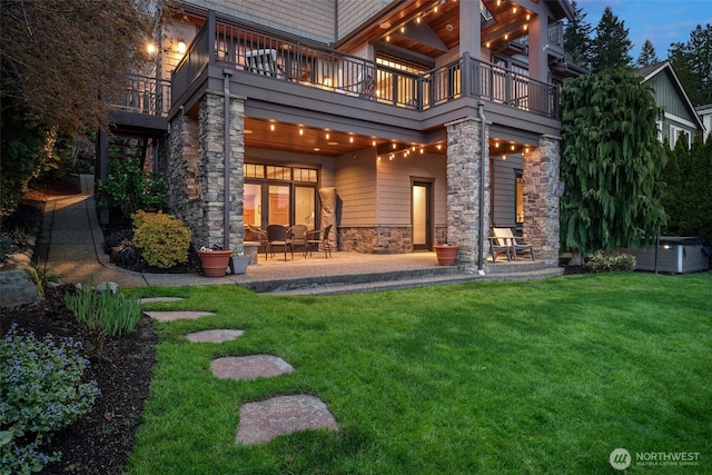 rear view of house featuring a yard, stone siding, a patio, and a balcony